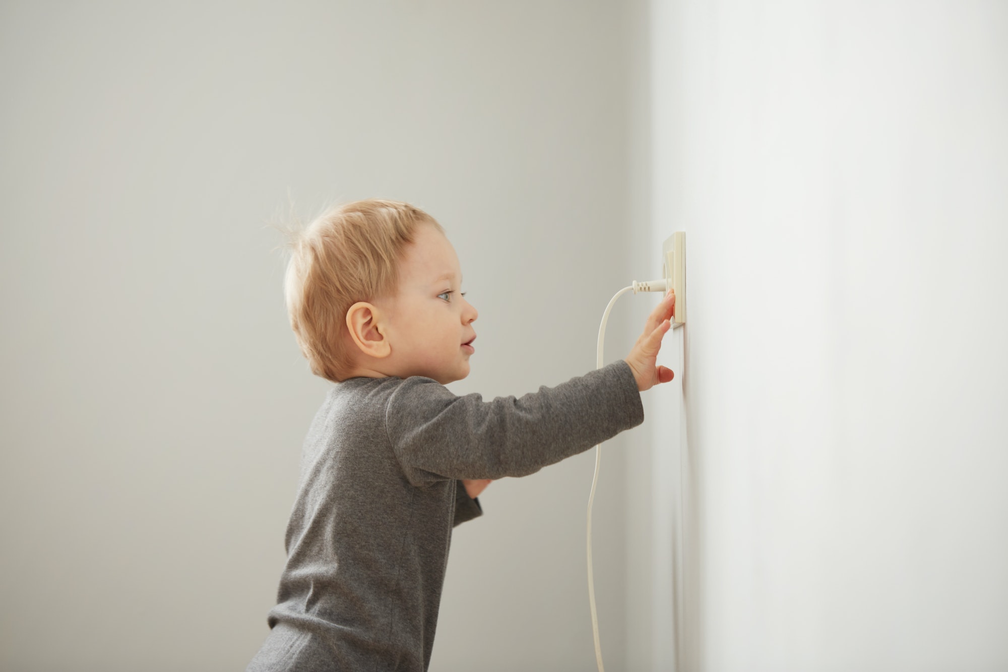 Curious little boy playing with electric plug. Trying to insert it into the electric socket. Danger